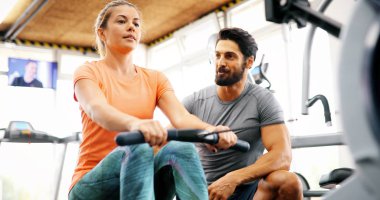 Genç ve güzel bir kadın spor salonunda antrenörle egzersiz yapıyor.