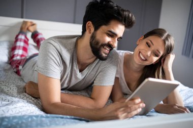 Mutlu çift tablet gibi görünüyor ve yatakta yatarken gülüyorlar.