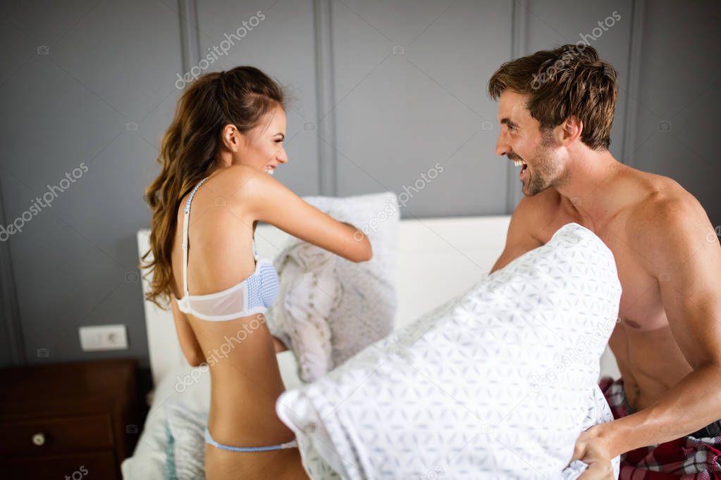 Happy young couple is having fun in bed. Enjoying the company of each other. Pillow battle