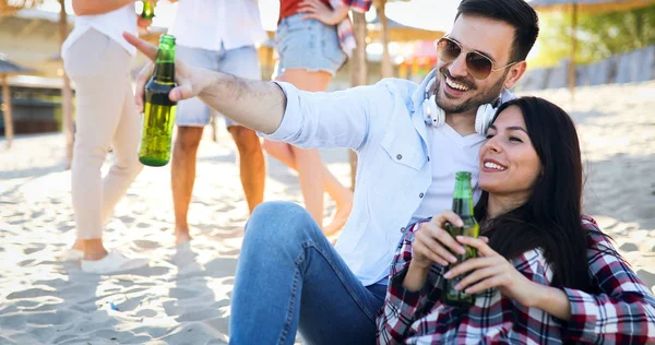 幸せな若いカップルはビールを飲んで 日没の間にビーチで楽しんでいます — ストック写真