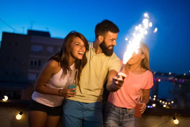 Bir grup arkadaş, kıvılcımlarla çatı partisinin tadını çıkarıyor. Eğlenen gençler