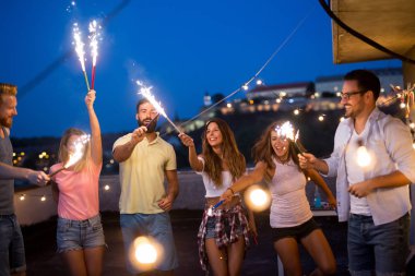Bir grup arkadaş, kıvılcımlarla çatı partisinin tadını çıkarıyor. Eğlenen gençler