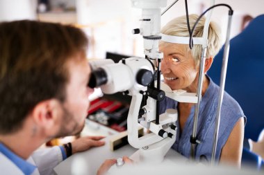 Yaşlı kadın göz doktoru kliniğinde görme testi yaptırıyor.