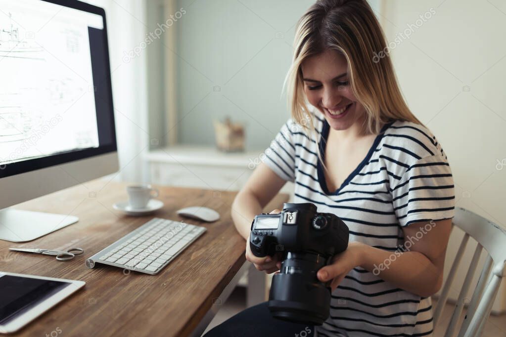 Young smiling beautiful designer holding digital camera at home