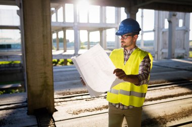 İnşaatta çalışan ve blueprint tutan yakışıklı mühendisi