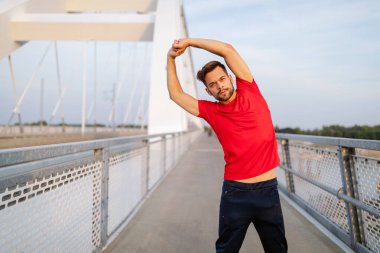 Yakışıklı genç adam dışarıda koşmadan önce ısınıyor.
