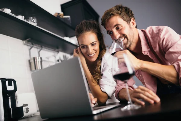 Young couple relaxing in kitchen with laptop and wine. Love, happiness, technology, people and fun concept.
