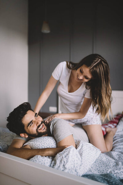 Beautiful young woman is doing her handsome boyfriend massage and smiling while they are resting at home