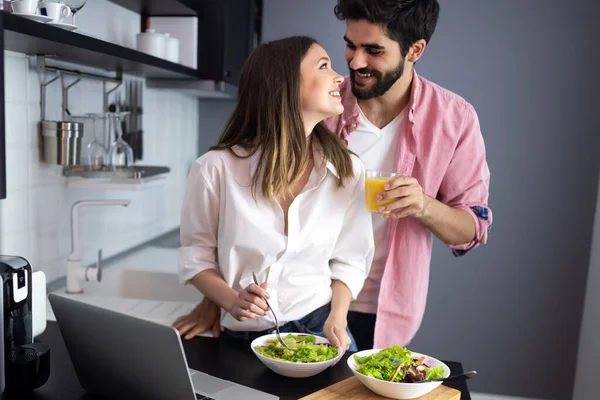 Beautiful young playful couple eating salad together at kitchen