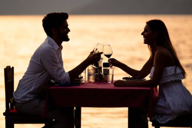 Genç çift, tropik bir tatil köyünde romantik bir gün batımı yemeği yiyor.
