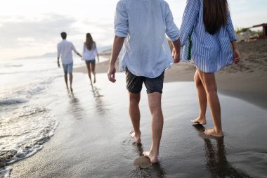 Bir grup arkadaş gün batımında sahilde yürüyor ve eğleniyorlar.