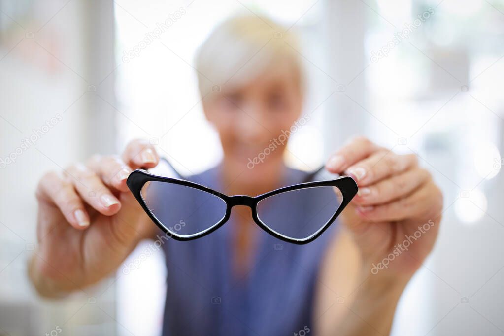 Pretty senior woman is choosing new glasses at optics store