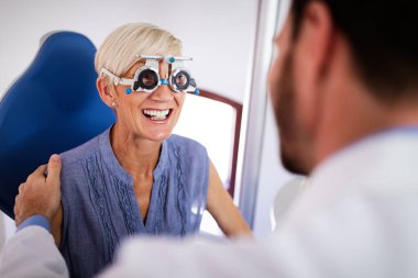 Yaşlı kadın göz doktoru kliniğinde görme testi yaptırıyor.