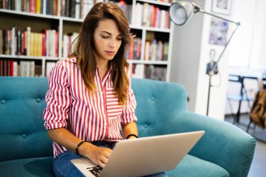 Kanepede otururken dizüstü bilgisayar kullanan mutlu bir kadın.