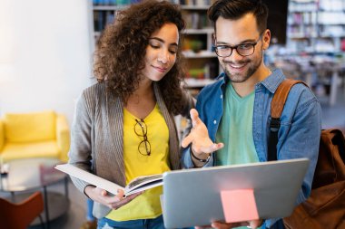 Üniversite öğrencileri kütüphanedeki görevleriyle işbirliği içinde. Kitap okuyan bir grup genç..