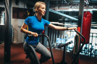 Spor salonunda egzersiz bisikletinde çalışan zinde bir genç kadın.