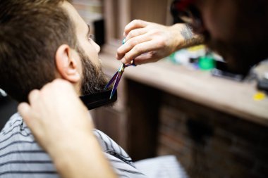 Berber berber dükkanında sakallı bir adamı tıraş ediyor.