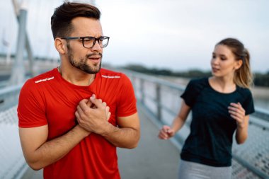 Young fit man feeling pain in heart during exercise outdoor