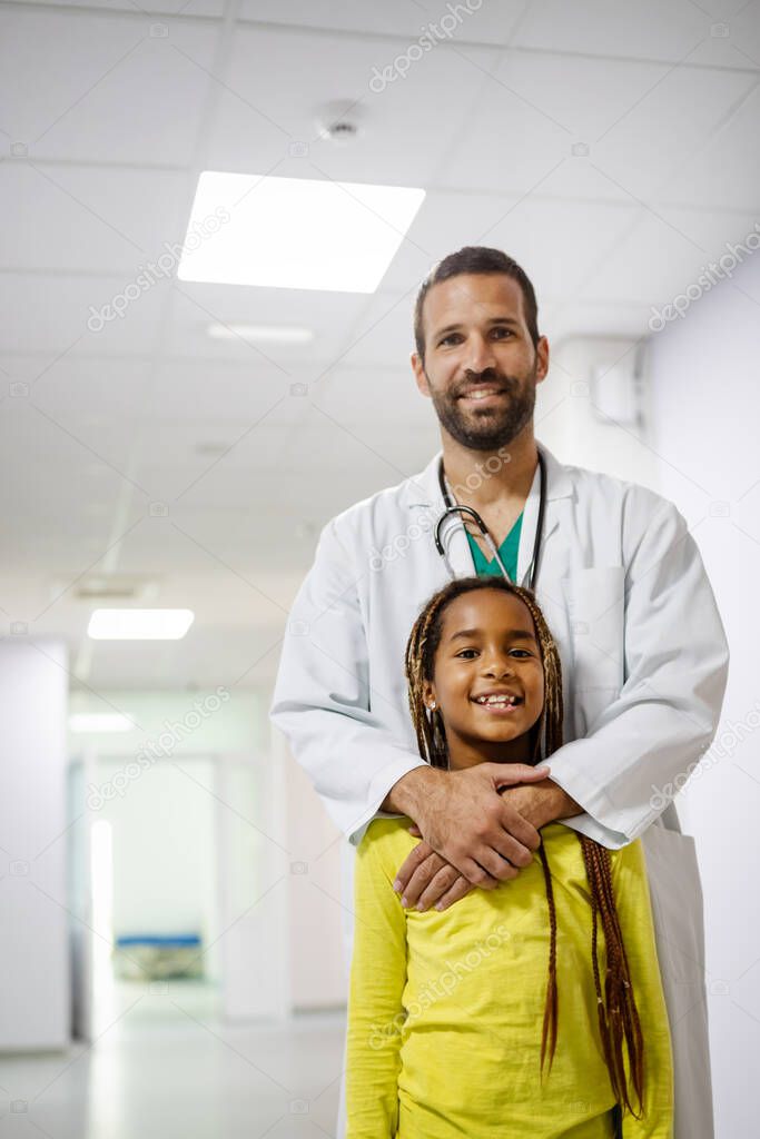 Handsome pediatrician doctor smiling with his little girl patient at hospital