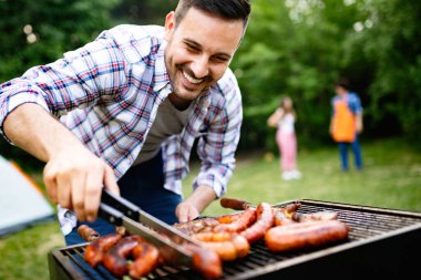 Handsome male preparing barbecue outdoors for friends clipart
