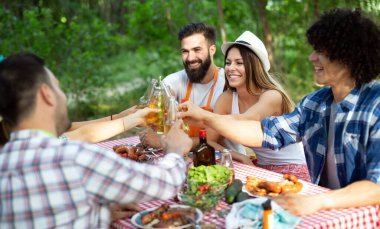 Bahçe barbeküsünde yemek yiyip kadeh kaldıran bir grup mutlu arkadaş. Evde gençlerin birlikte yemek yediği mutluluk kavramı.