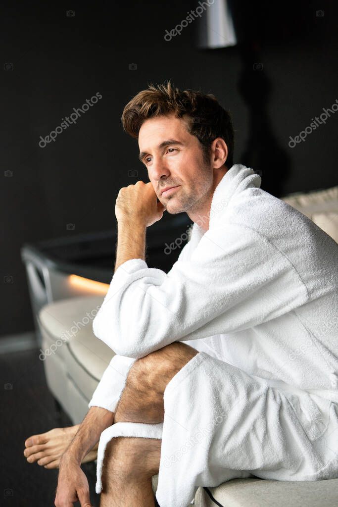 Young handsome man in the morning thinking while sitting in a hotel room in a robe