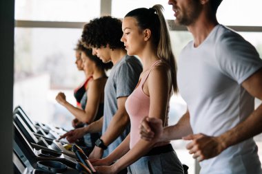 Spor salonunda koşu bandında koşan bir grup sağlıklı genç.