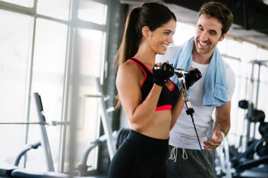 Spor salonunda antrenörüyle antrenman yapan sağlıklı bir kadının portresi.