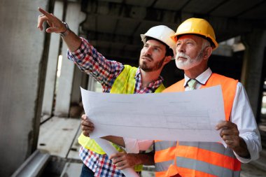 İnşaat alanı kontrol belgeleri ve iş akışı üzerine grup halinde çalışan mimarlar ve mühendisler.