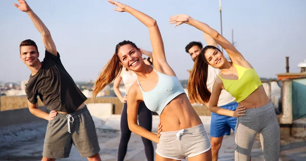 Group of happy fit people friends exercising together outdoor on rooftop. Sport, healthy life concept