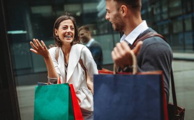 Birlikte alışveriş yapmayı seviyoruz. Güzel, genç, sevgi dolu bir çift ellerinde alışveriş çantalarıyla sokakta yürüyor.