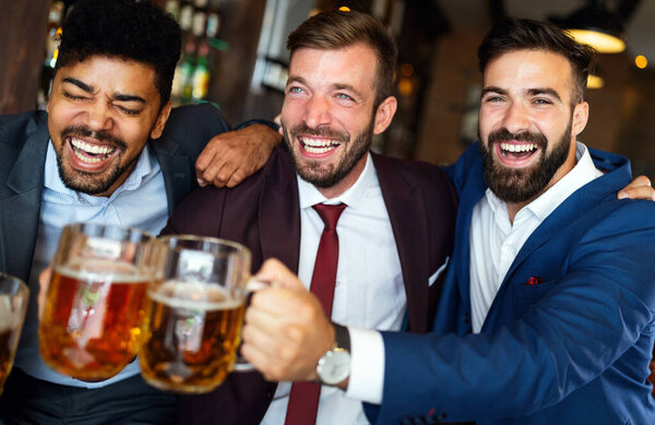 Cheerful old friends, business man having fun and drinking beer at bar counter in pub.