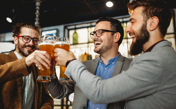 People, men, leisure, friendship and celebration concept. Happy business male friends drinking beer and clinking glasses at bar or pub