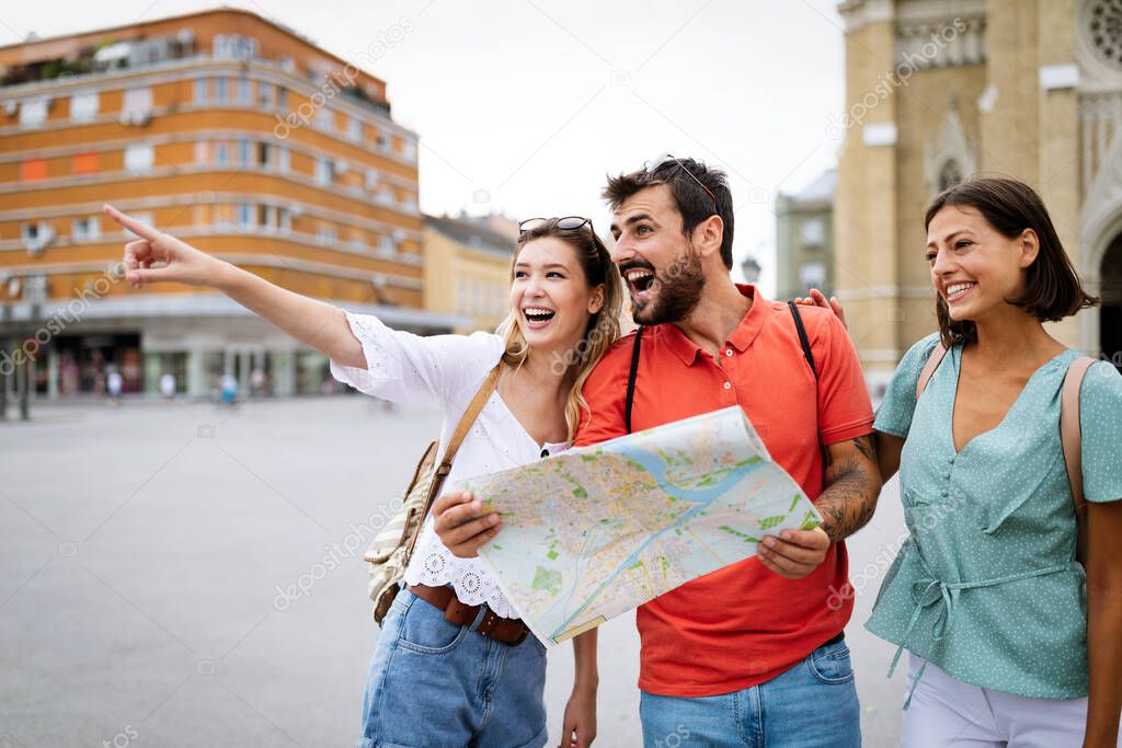 Holidays and tourism concept. Happy friends looking into tourist map in the city