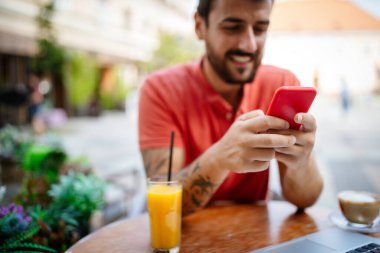 Açık kafedeki akıllı telefondan internette gezinen mutlu genç adam..