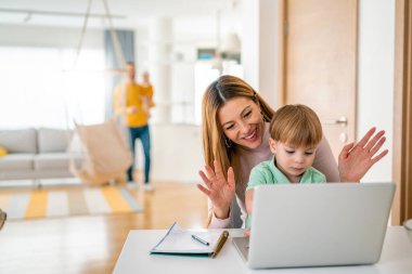 Evde bilgisayar kullanarak mutlu genç bir aile, canlı yayında el sallıyor.
