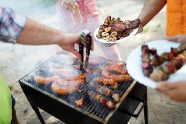 Portatif bir barbeküde baharatlı sosisli kömürlerin üzerinde ızgara et seçimi.