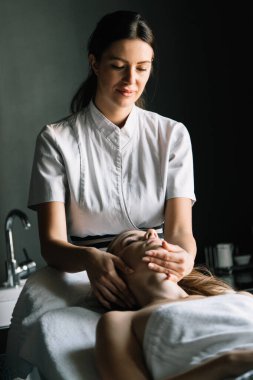 Masör spa salonunda genç kadın vücuduna masaj yapıyor.