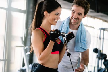 Spor salonunda antrenörüyle antrenman yapan sağlıklı bir kadının portresi.