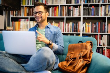 Gülümseyen erkek öğrenci kütüphanede çalışıyor ve öğreniyor.