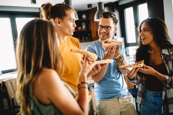 Neşeli çok ırklı arkadaşlar evde pizza yerken eğleniyorlar.