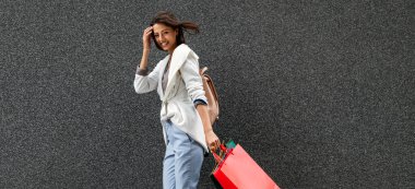 Çok mutlu, genç ve enerjik bir kadın. Günlük giysiler içinde, alışveriş torbalarıyla.