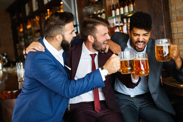 Cheerful old friends, businessmen having fun and drinking beer at bar counter in pub.