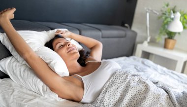 Kadın uyandıktan sonra yatakta geriniyor, bir güne mutlu ve rahat giriyor iyi geceler uykusundan sonra