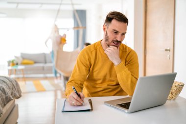 Evde dizüstü bilgisayar kullanarak çalışan yakışıklı, modern erkek tasarımcı.