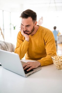 Evde dizüstü bilgisayarla çalışan hayal kırıklığına uğramış genç iş adamı.