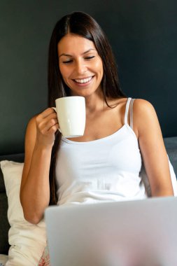 Mutlu genç bir kadın çalışıyor, evde dizüstü bilgisayarla web sörfü yapıyor. İnsanlar, teknoloji, ev kavramı