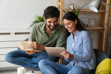 Mutlu genç çift evde dinleniyor. Kitap ve tablet bilgisayarda bir şeyler okunuyor.
