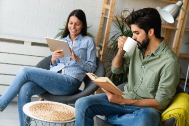 Mutlu genç çift evde dinleniyor. Kitap ve tablet bilgisayarda bir şeyler okunuyor.