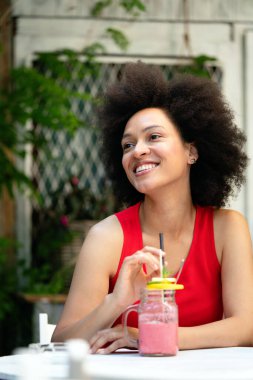 Dışarıda poz veren seksi Afrikalı kadının hayat tarzı portresi. Yazlık kafede ve smoothie kokteyli içerken. Gülümse ve eğlen..
